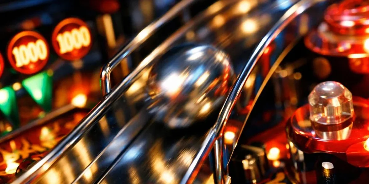 Close-up de uma bola de pinball de aço em um playfield colorido, destacando a natureza mecânica e física do jogo.