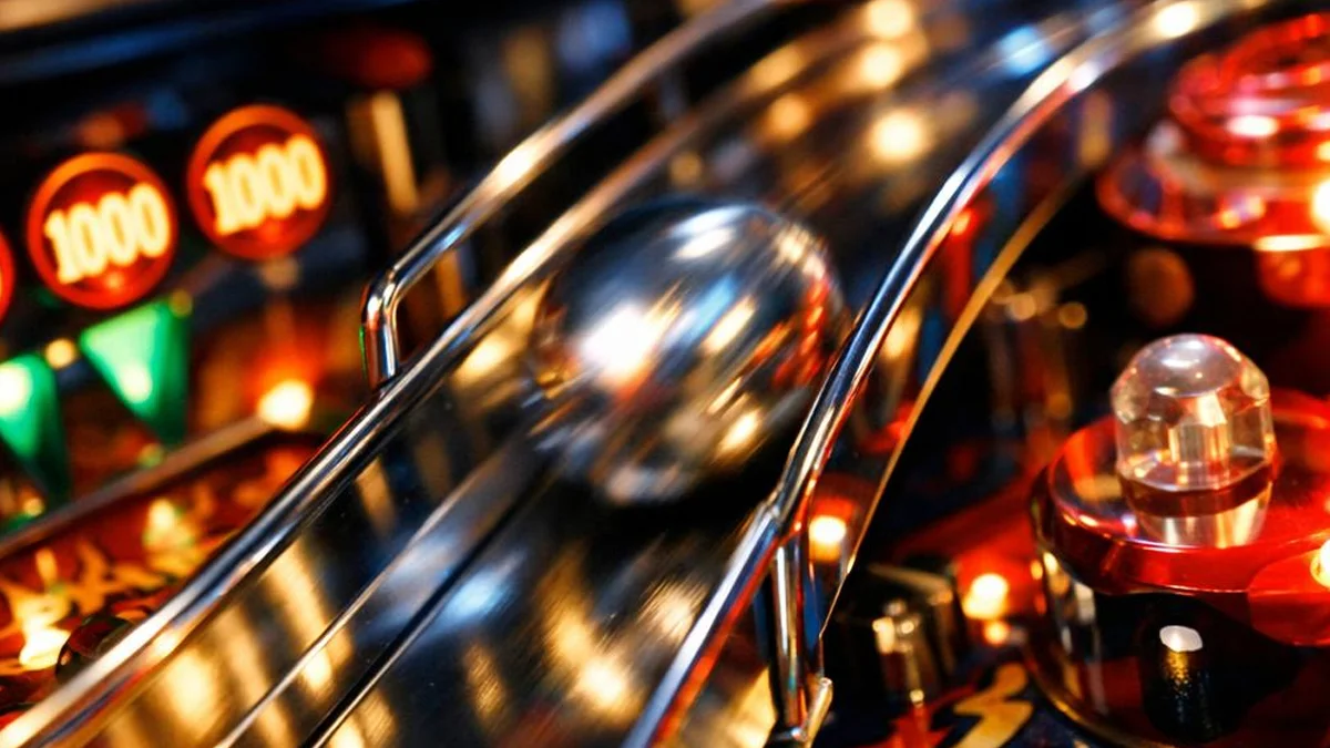 Close-up de uma bola de pinball de aço em um playfield colorido, destacando a natureza mecânica e física do jogo.